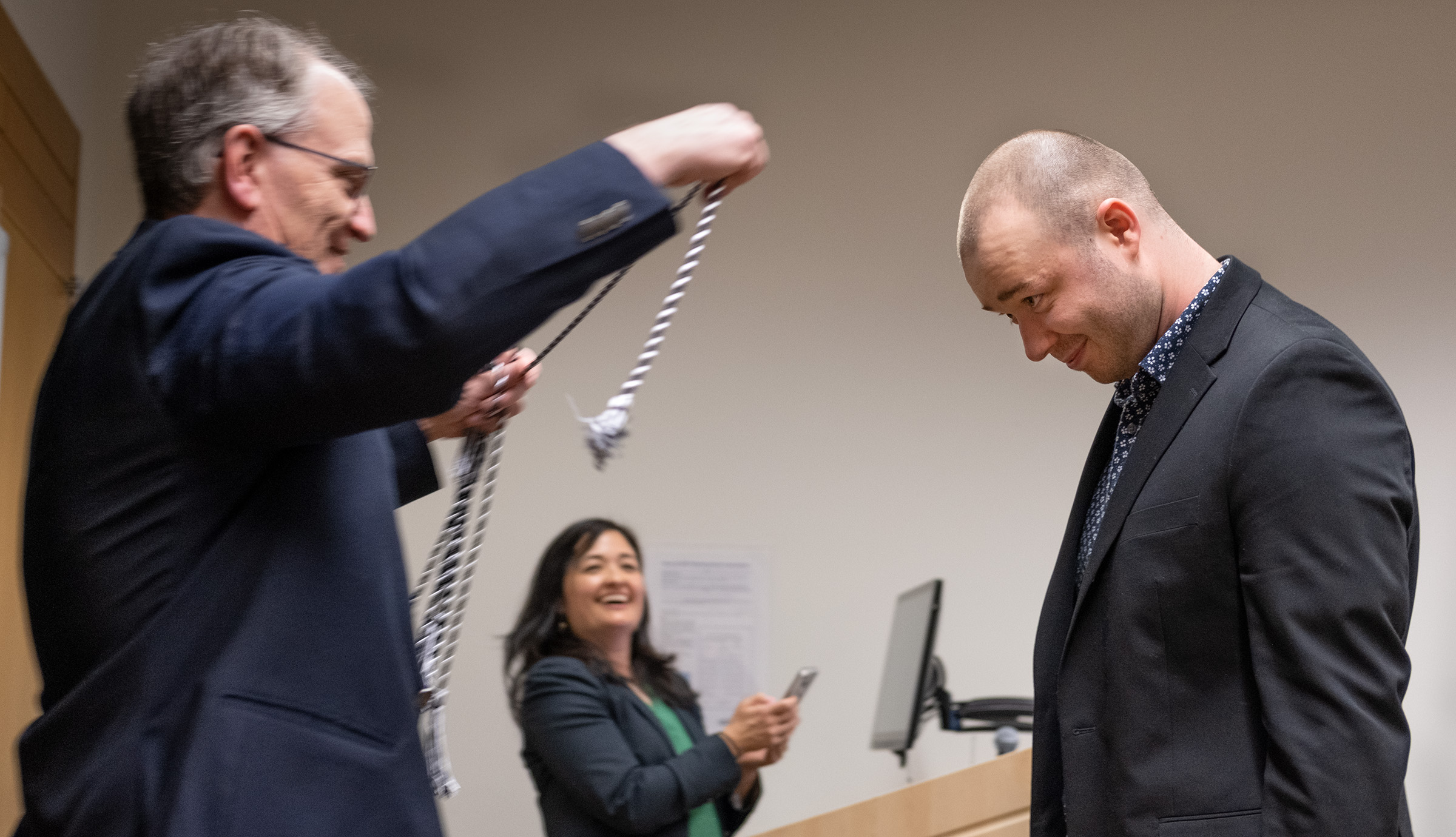 Prof. Mike Stanton drapes a honor cord around the neck of senior journalism major Hudson Kamphausen as Department Head Marie Shanahan looks on.