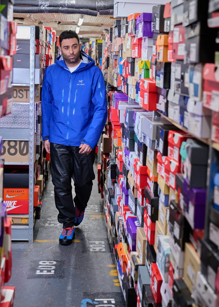 Man in blue jacket walks past rows of colorful shoe boxes